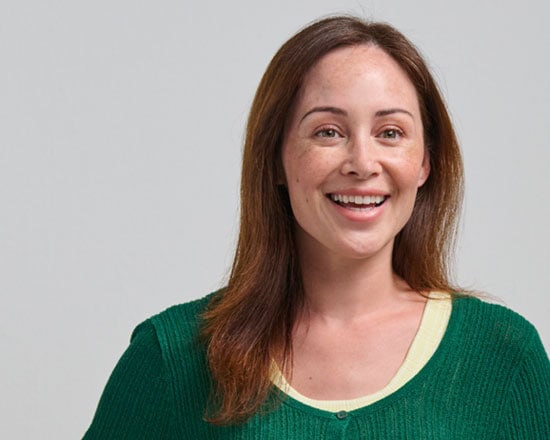Smiling woman with brown hair wearing a green sweater, representing health and wellness, in a professional setting.